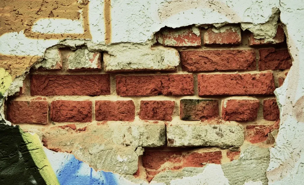 Wałek z białą farbą oraz próbka wzorzystej tapety na drewnianym stole, symbolizujące wybór kolejności prac remontowych.